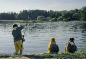 Family casting rods together at a mountain lake during a sunny fishing day