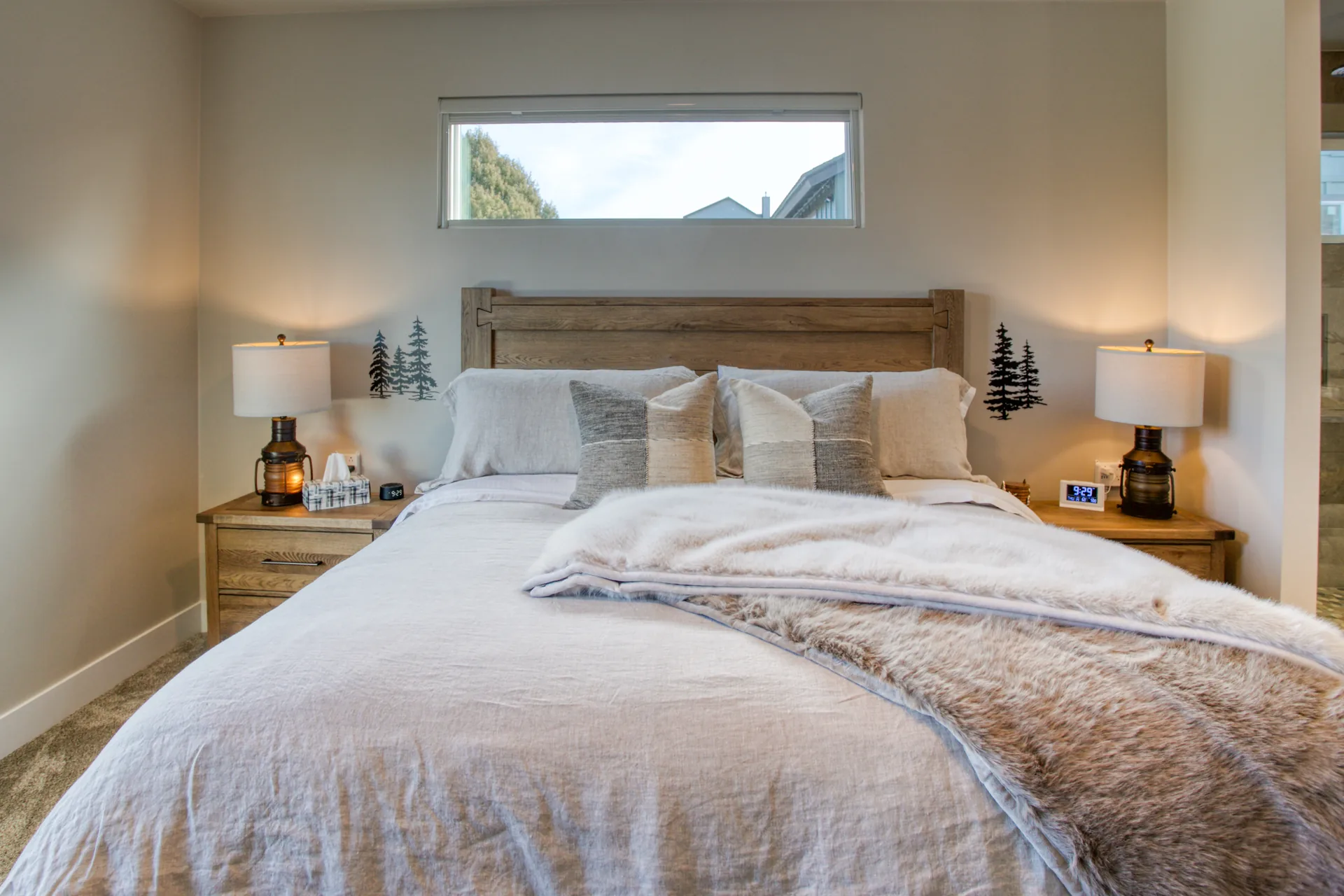 Primary bedroom with king bed, rustic wood headboard, and tree-line window view