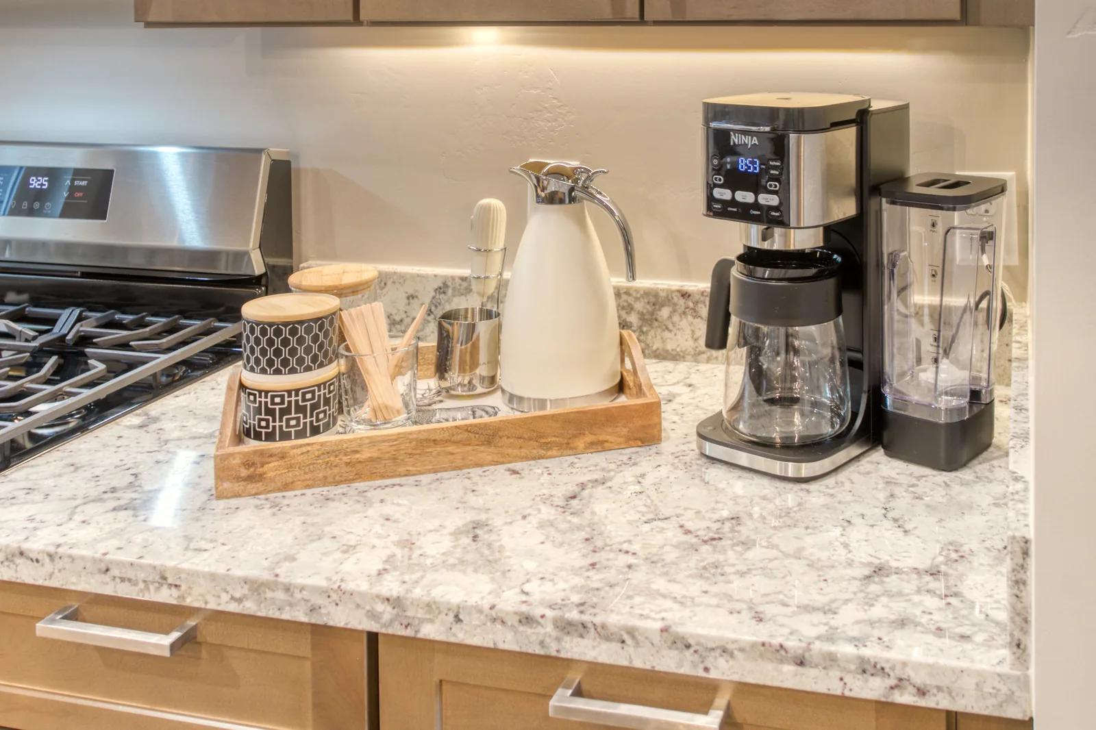 Stocked coffee bar with drip coffee maker, electric kettle, and canisters on granite counter