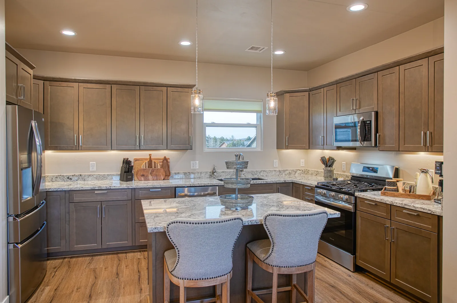 Kitchen island with granite counters, pendant lights, and stainless French-door refrigerator