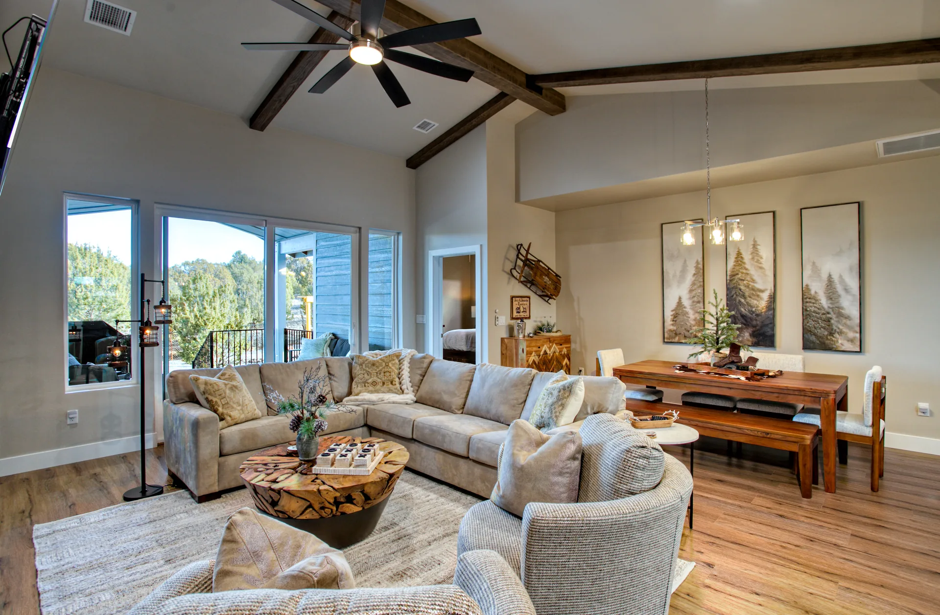 Open-plan living and dining room with sectional sofa, wood beams, and forest views at Bluff Retreat